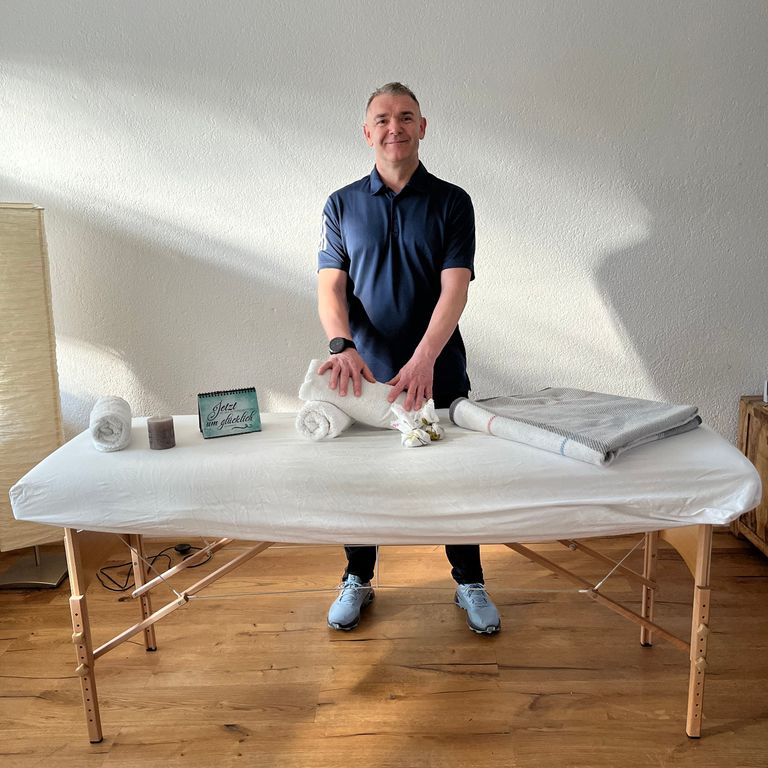 Peter hinter einer Massageliege mit Handtüchern und Massageöl